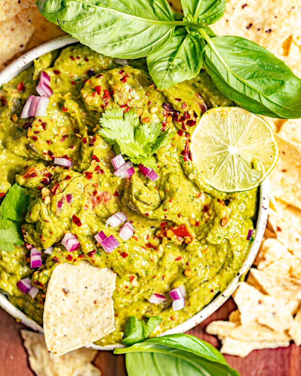 guacamole in a bowl surrounded by tortilla chips and garnished with fresh basil.