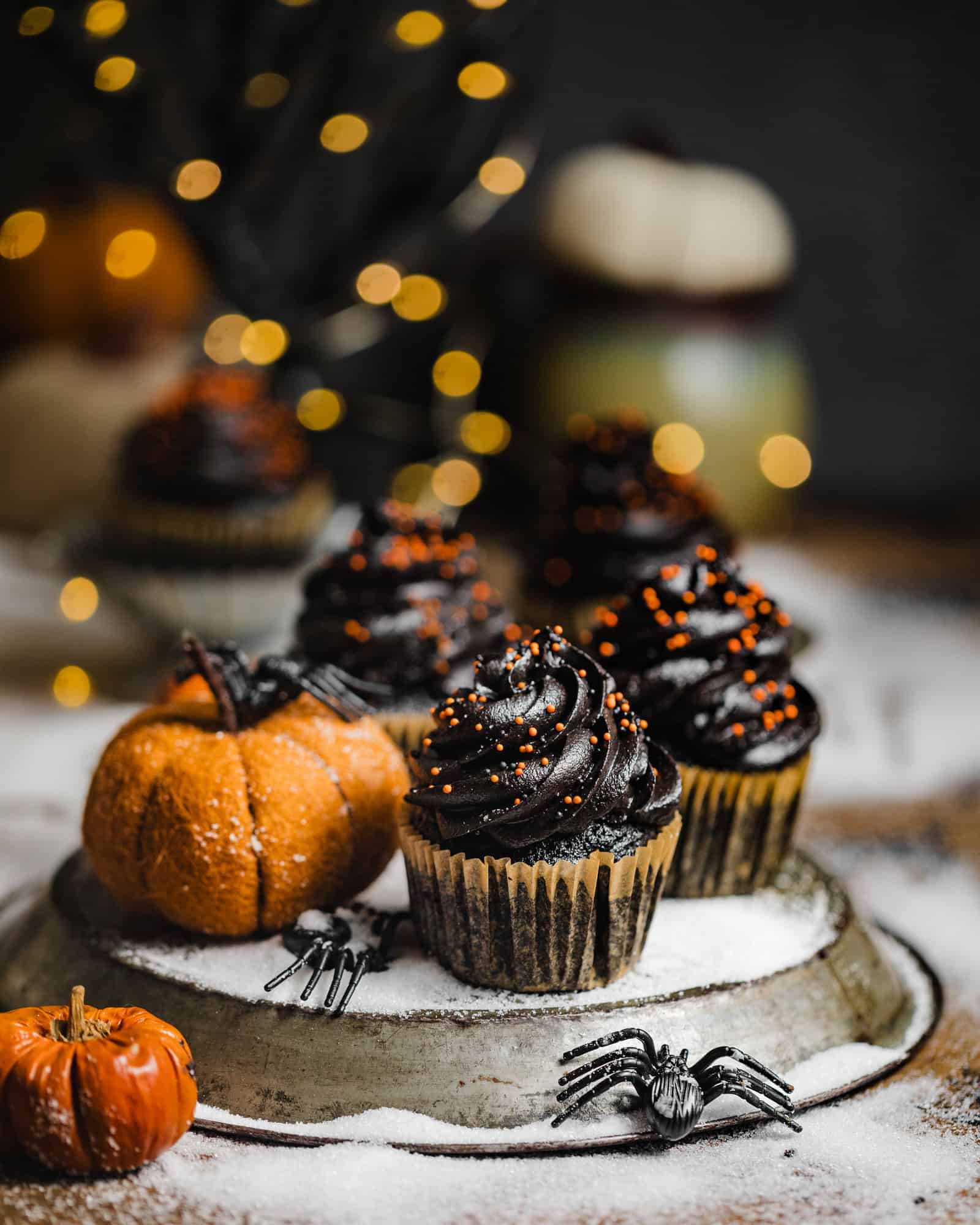 three black velvet cupcakes on a plate with a pumpkin and fake spiders.