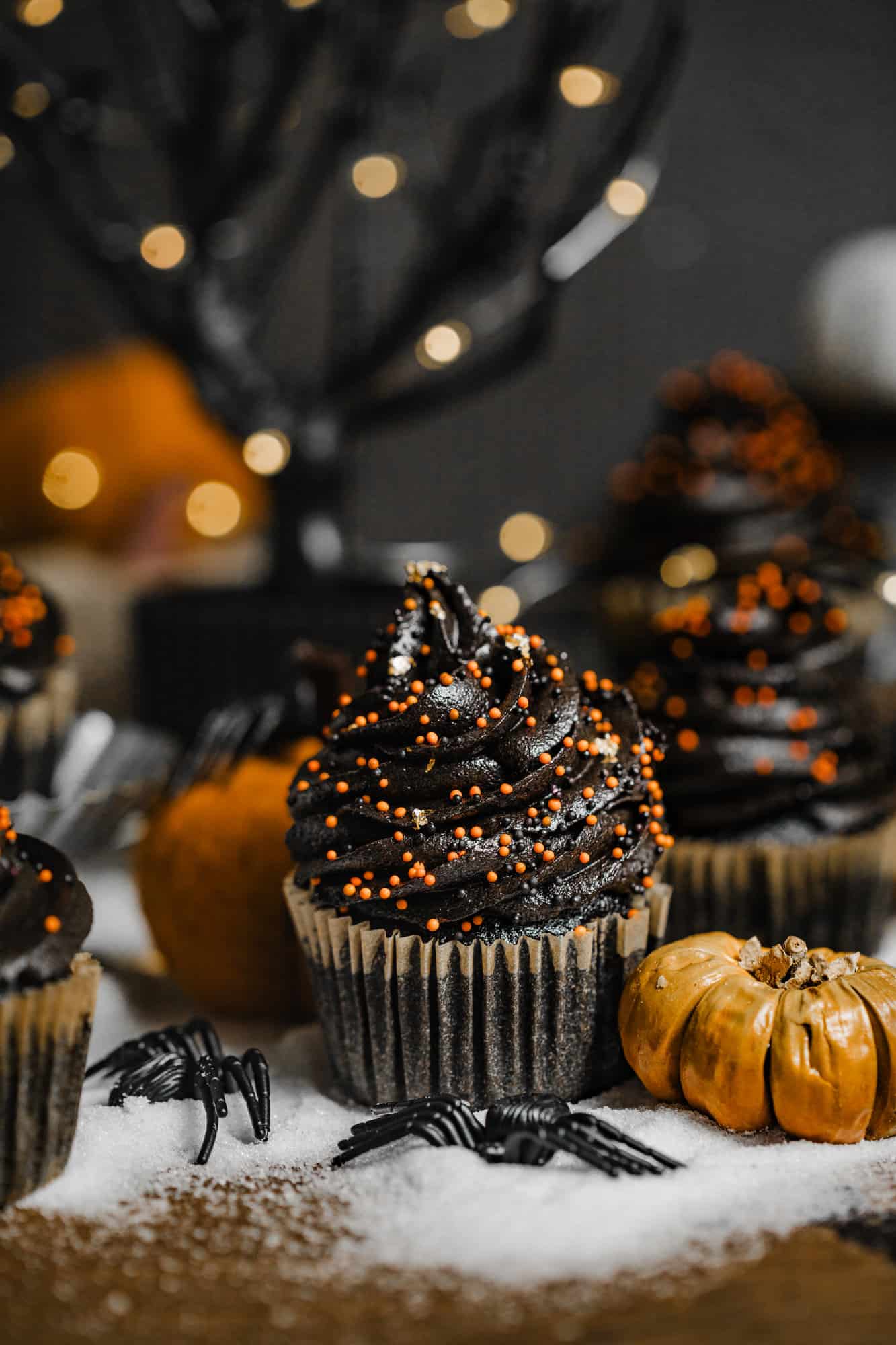a black velvet cupcake in front of a black tree with pumpkins and fake spiders.