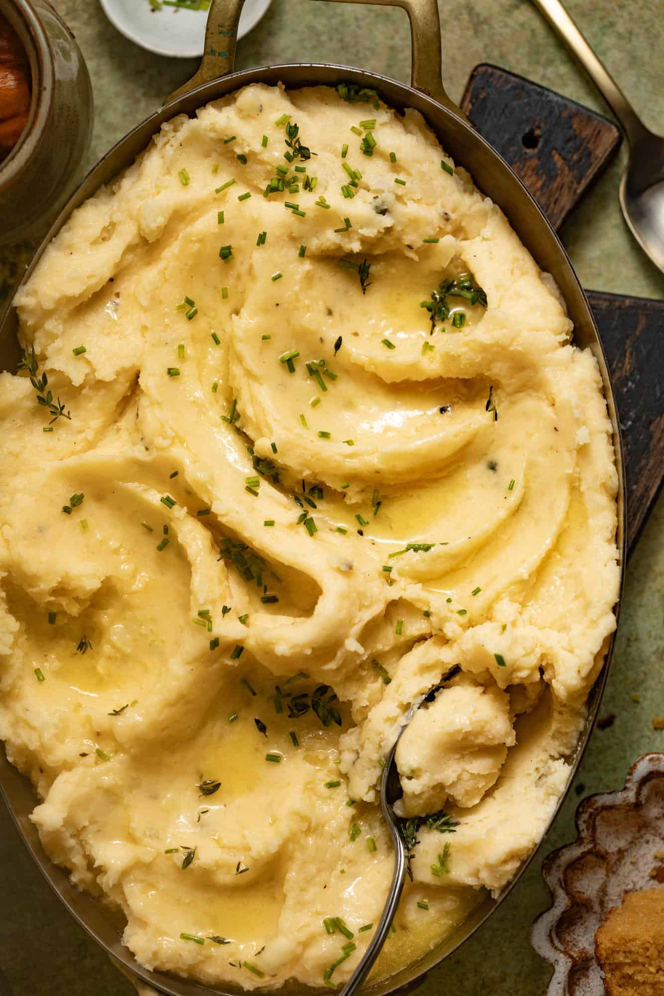 A spoon in a serving dish of cheesy mashed potatoes topped with butter.