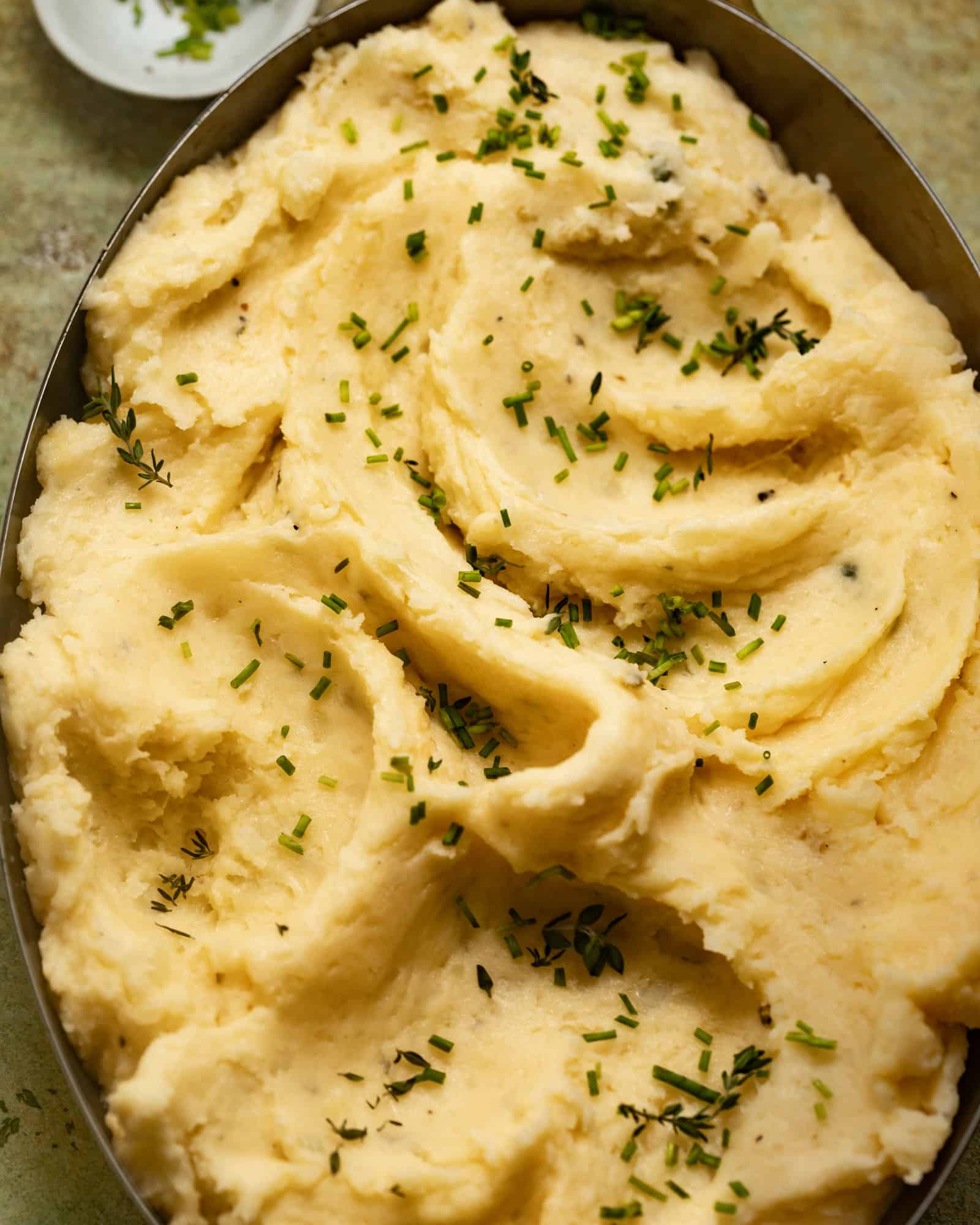 Cheesy mashed potatoes in a baking dish topped with fresh chives.