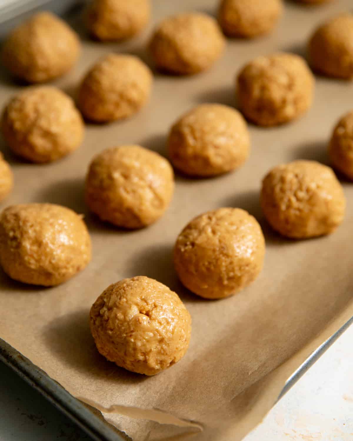 Peanut butter truffle filling in balls on a parchment lined sheet pan.