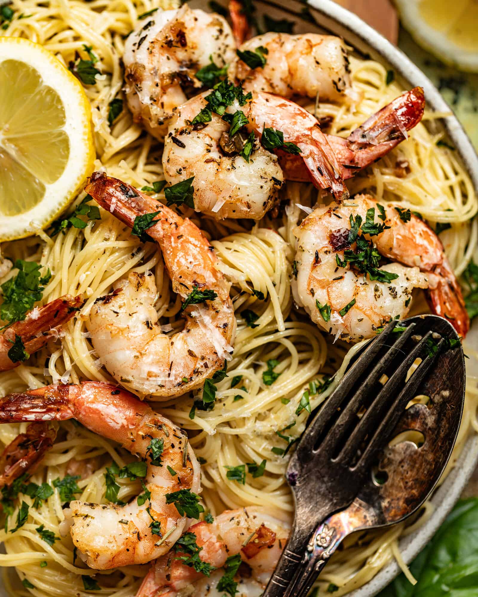 Shrimp scampi with lemon wedges over pasta and fresh parsley.
