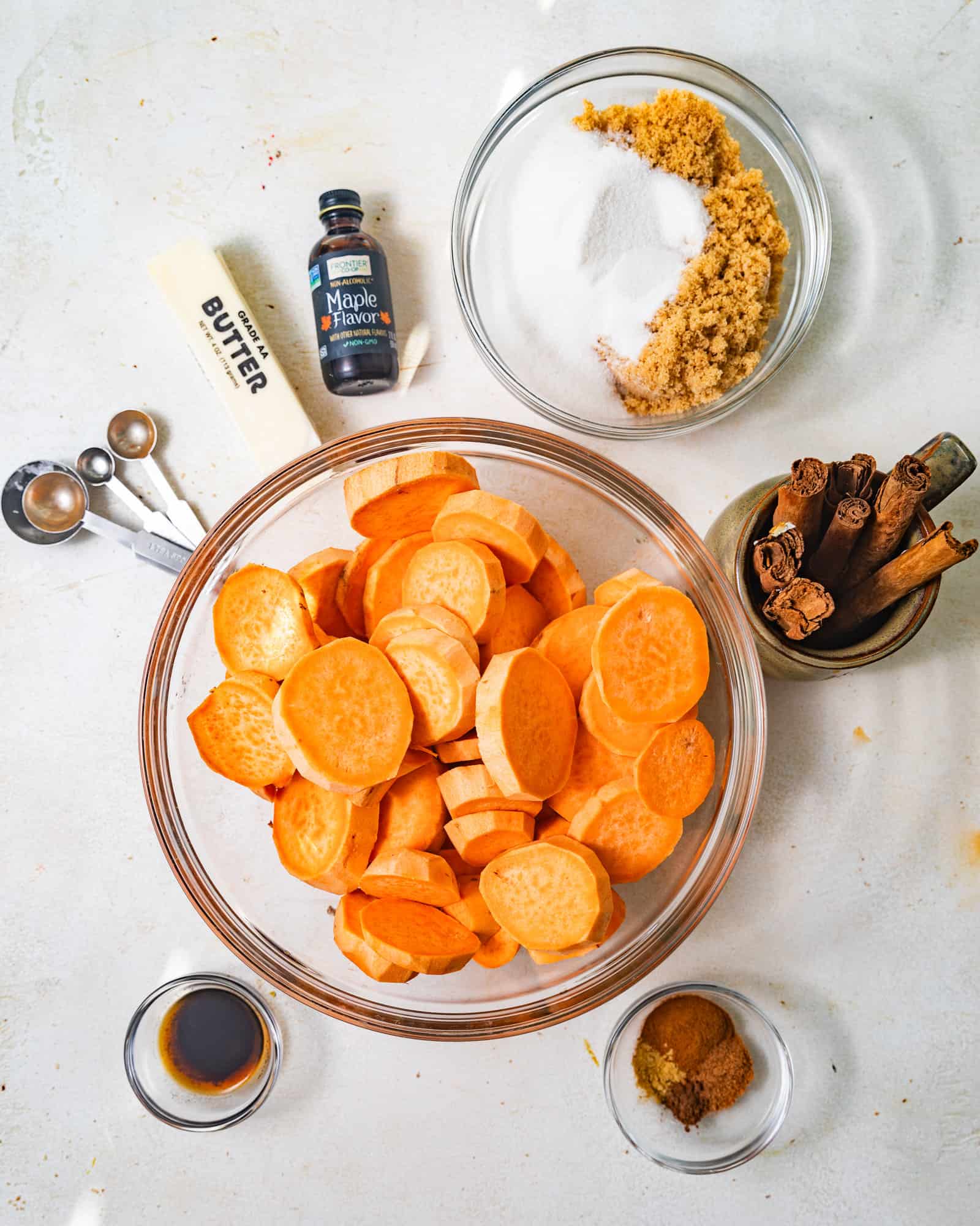 photo of ingredients needed to make candied yams - sugar, brown sugar, sweet potatoes, vanilla extract, maple extract, cinnamon, salt, nutmeg, ginger, and butter