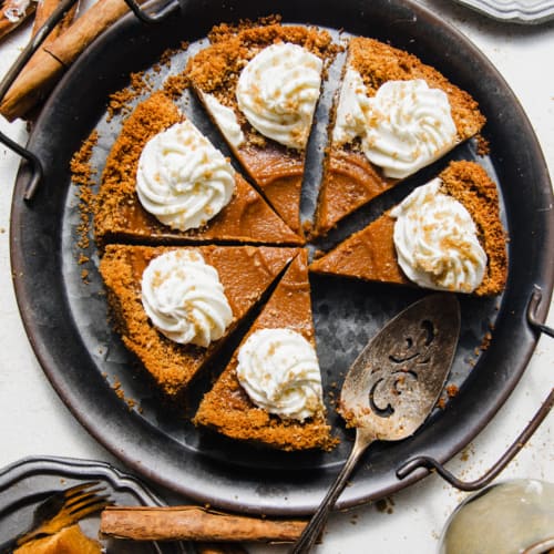 sliced sweet potato pie with graham cracker crust on a silver platter topped with whipped cream