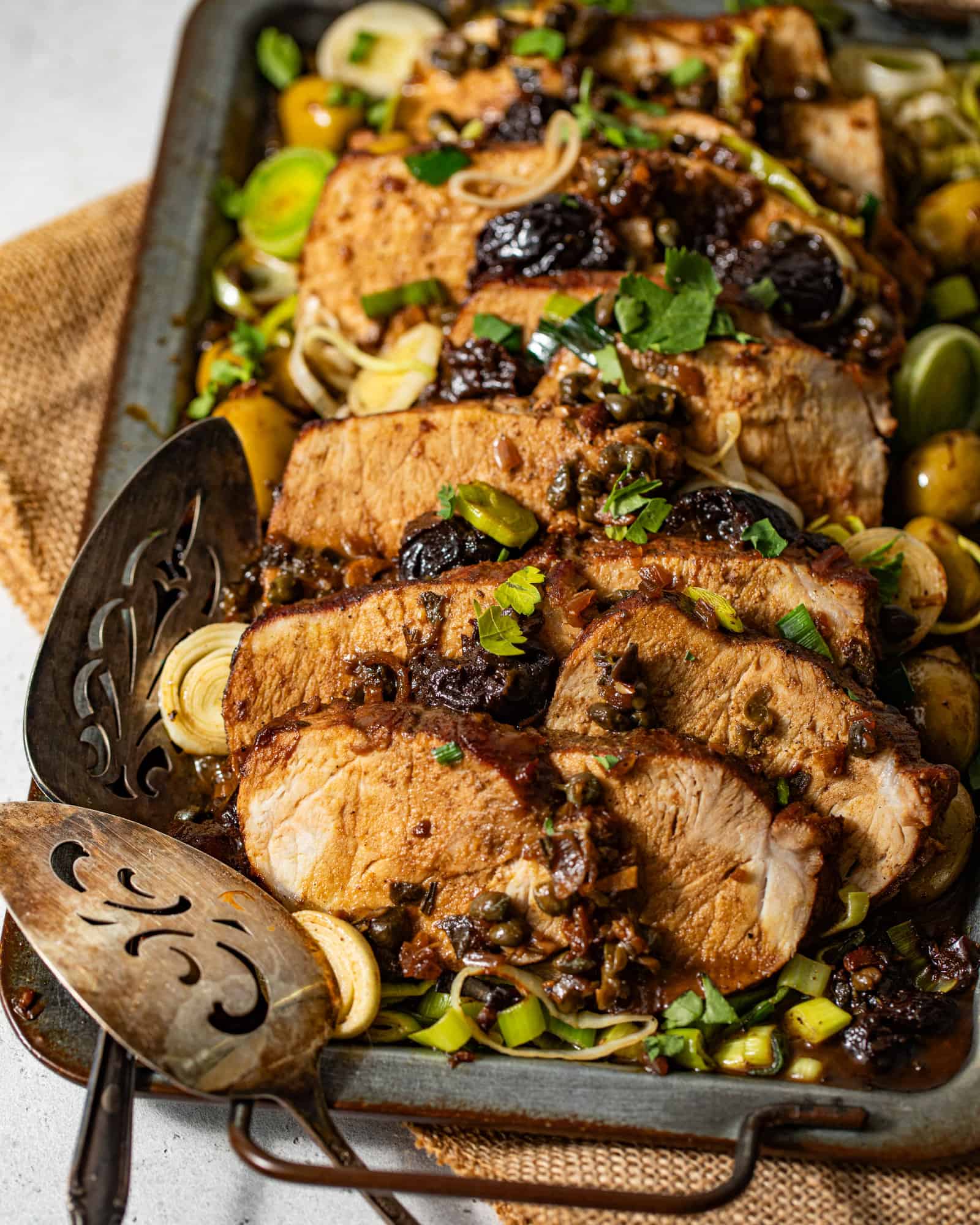pork marbella on a serving dish with prunes, capers, leeks, and olives on top