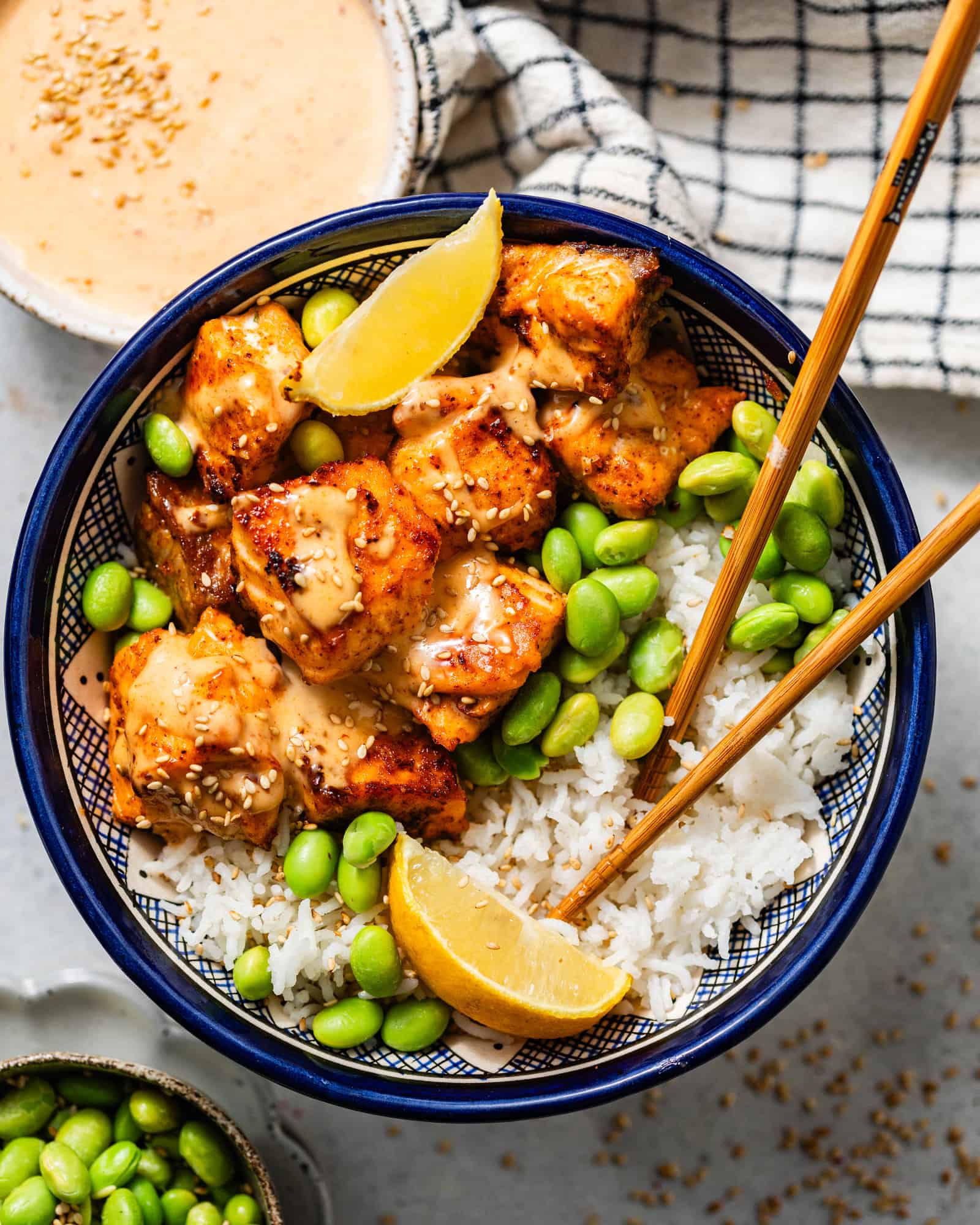 overhead photo of salmon bites in a bowl with edamame, lemon wedges, rice, and a pair of chopsticks