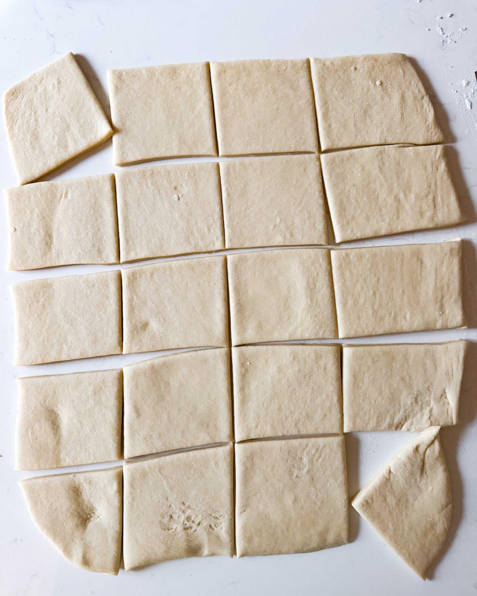 beignet dough cut into 3 inch squares on a white surface