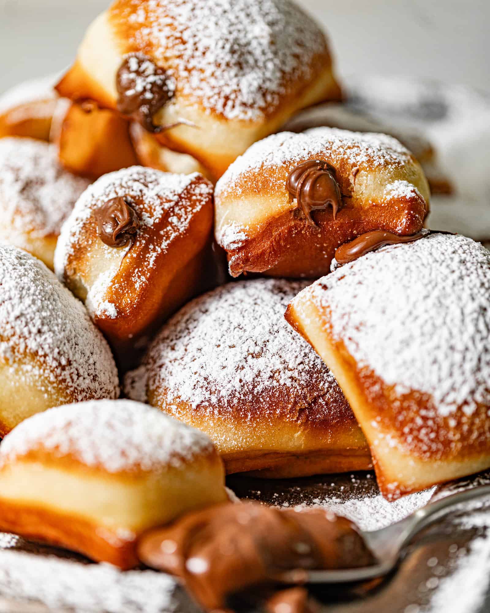 nutella beignets stacked on top of each other and covered in powdered sugar with nutella oozing from the center.