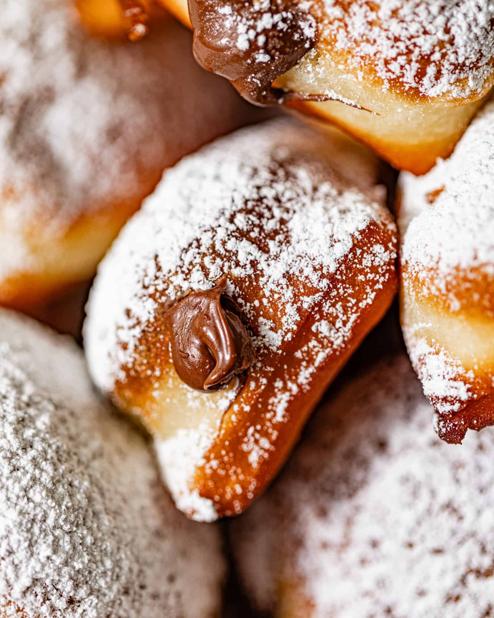 up close photo of nutella beignets topped with powdered sugar and nutella coming out of the beignet.