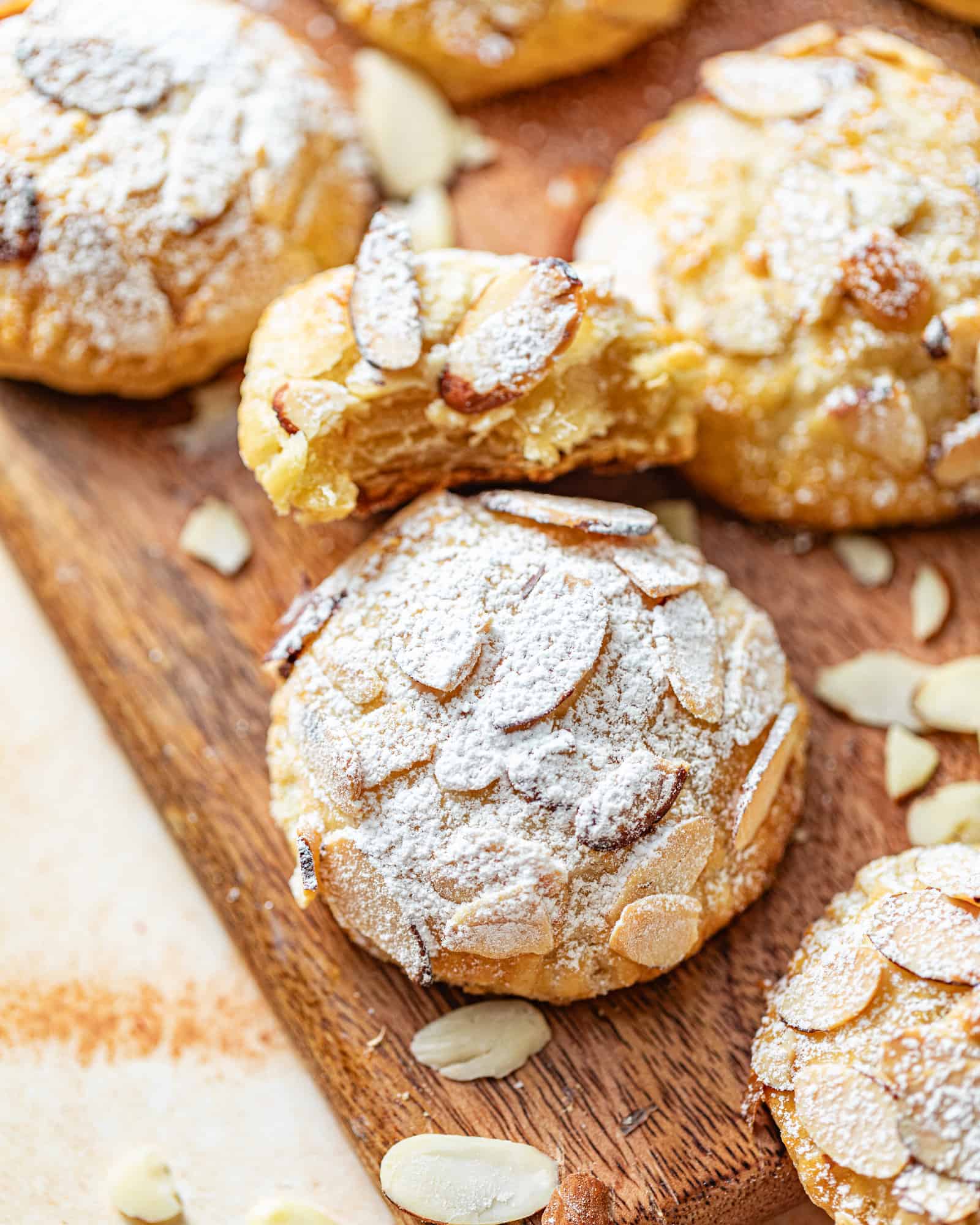 almond croissant cookies on a tray with sliced almonds and powdered sugar.