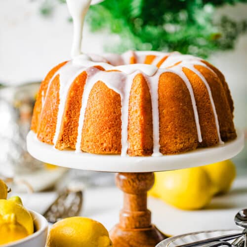 lemon glaze being poured onto a lemon bundt cake on a cake stand.