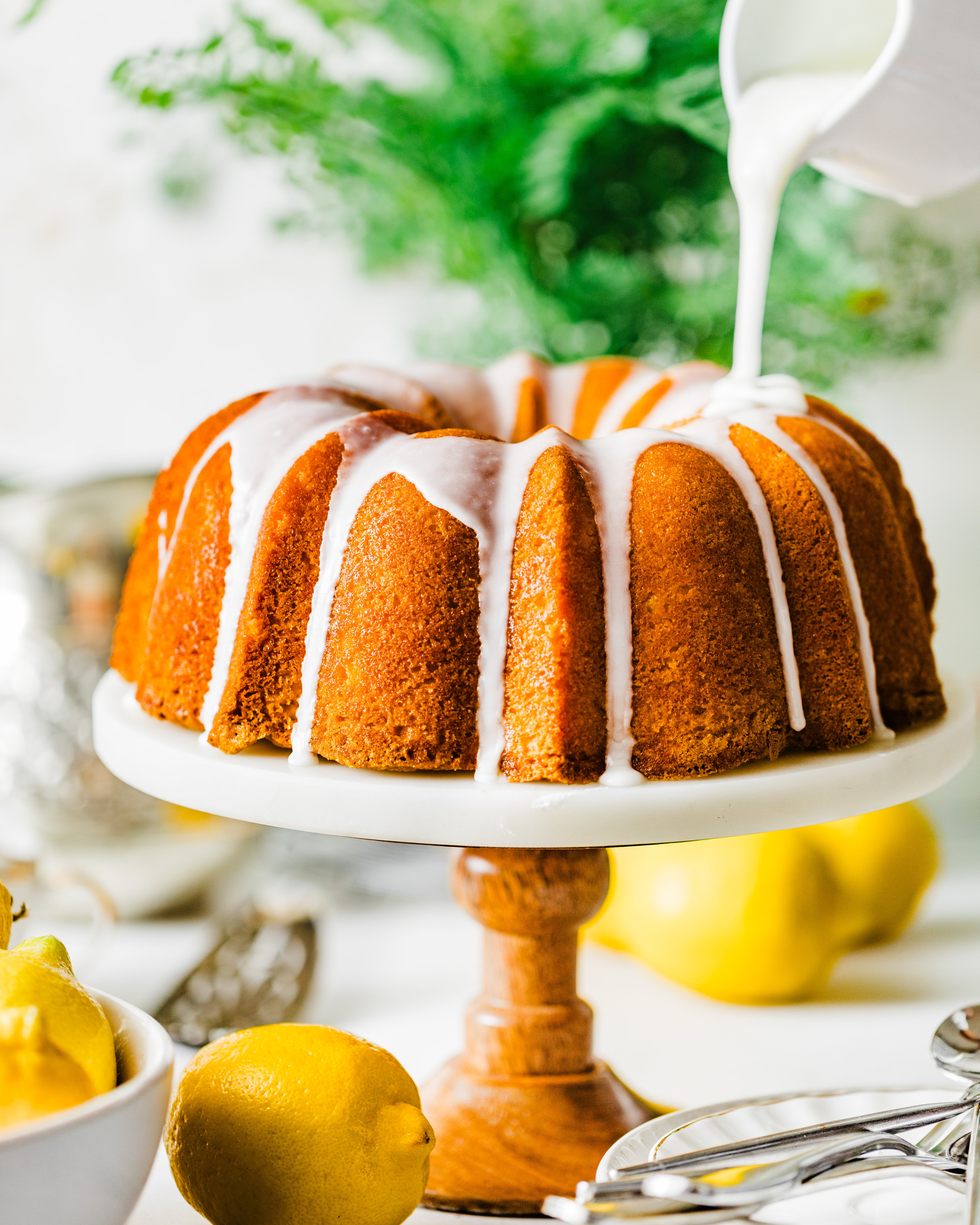 lemon glaze being poured onto a lemon bundt cake on a cake stand.