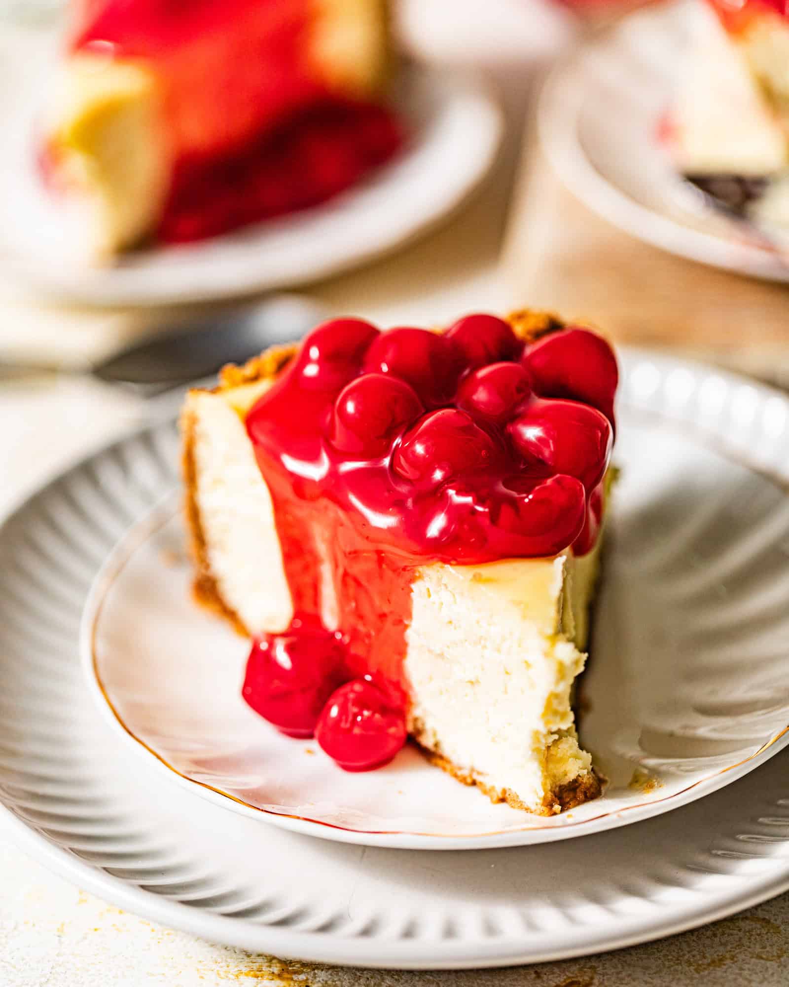 a slice of cherry cheesecake on a white plate covered in cherry pie filling.