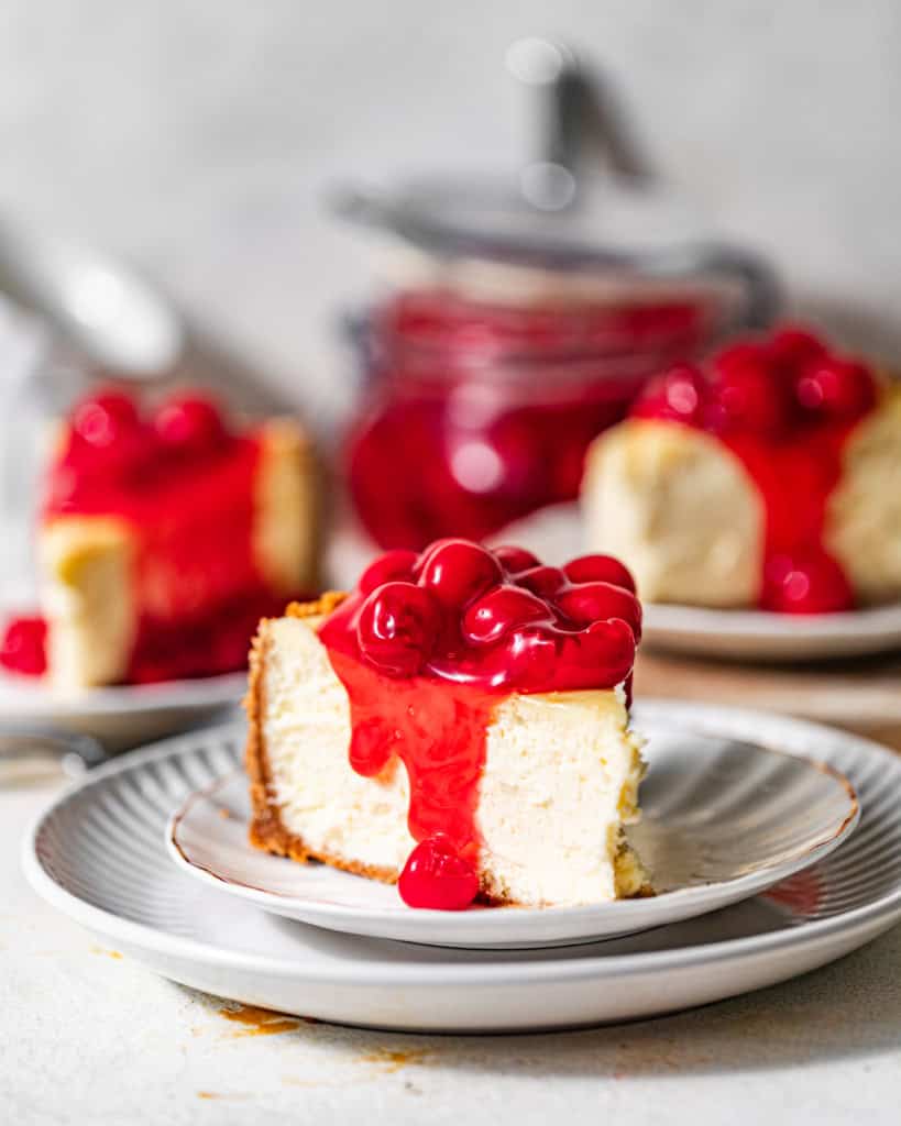 slices of cherry cheesecake on white plates covered in cherry sauce.