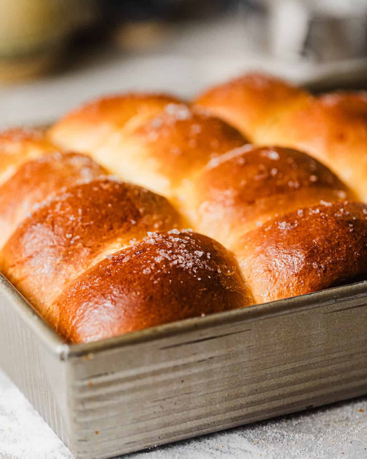 brioche dinner rolls in a baking dish with flaky sea salt and melted butter on top.