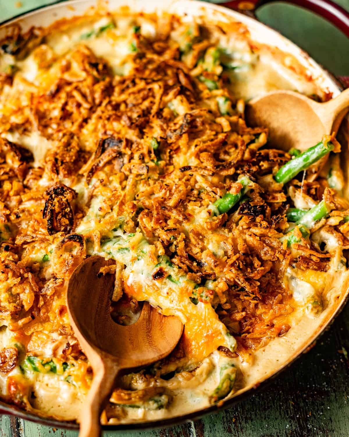 up close photo of green bean casserole in a skillet with serving spoons. 