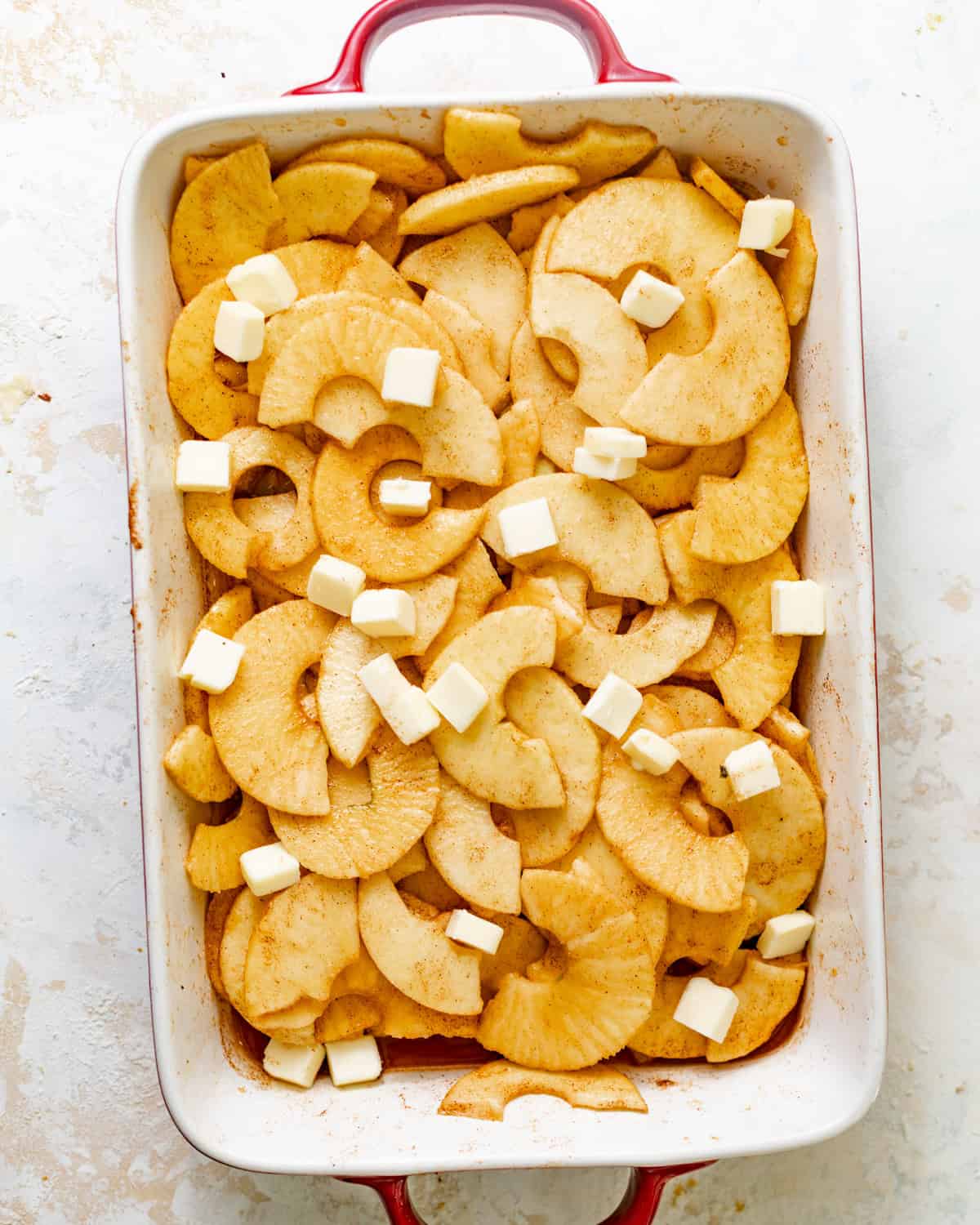 apple cobbler filling in a baking dish topped with cubed butter.