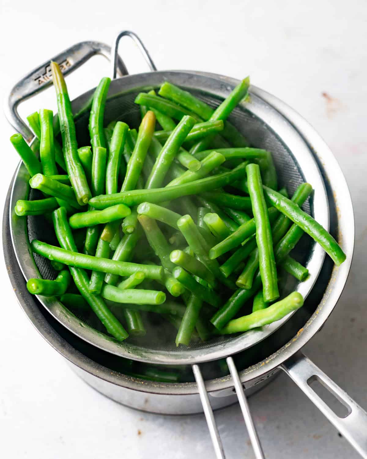 blanched green beans in sieve over a saucepan. 