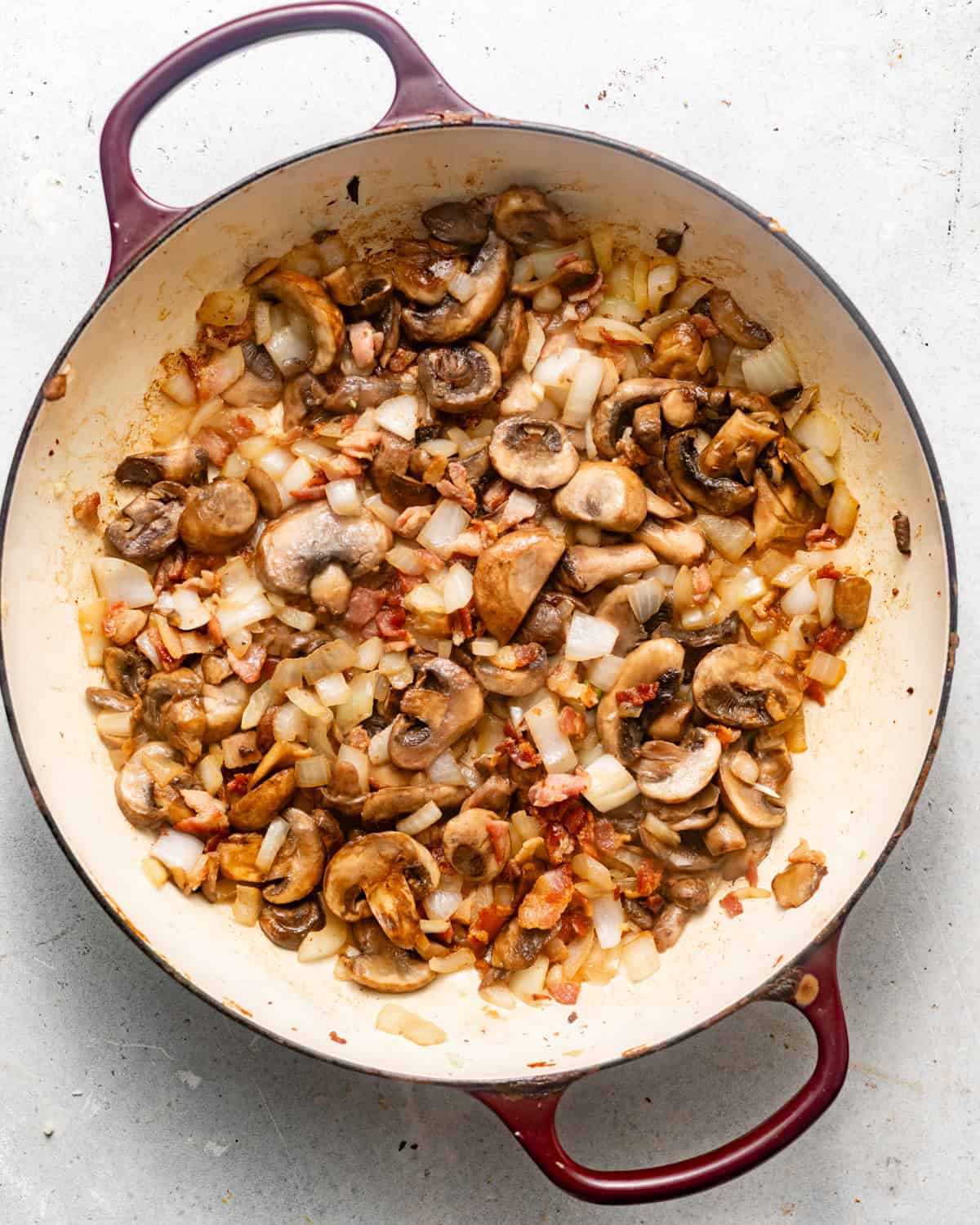 bacon, onions, and mushrooms being cooked in a large pan. 