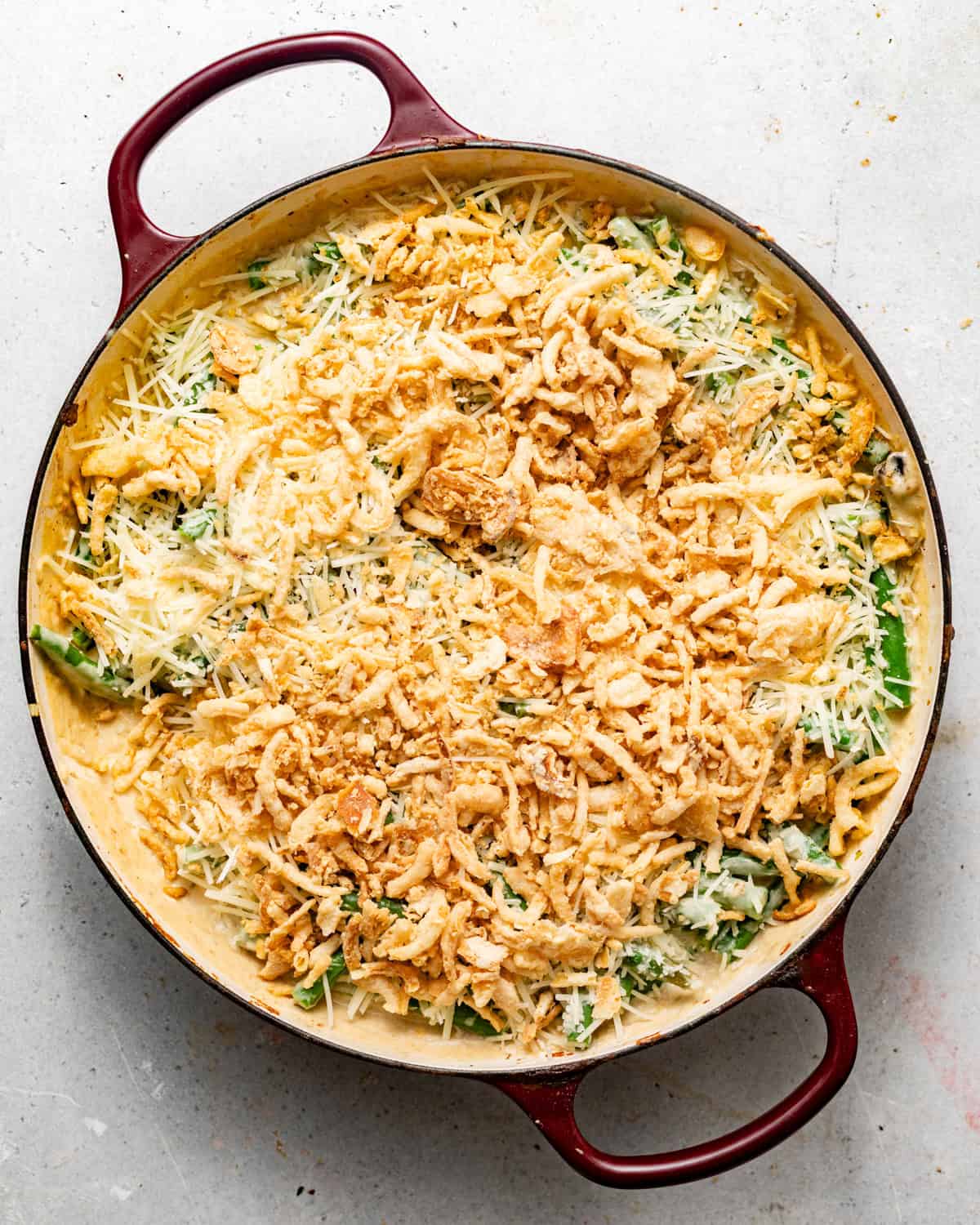green bean casserole assembled in a large pan and topped with parmesan cheese and french fried onions.
