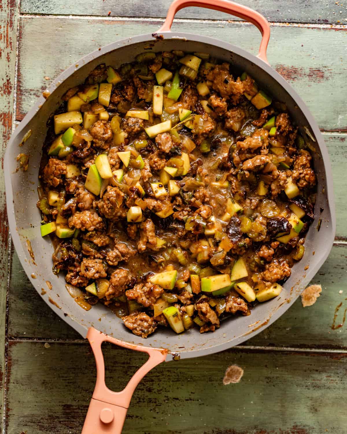 sausage mixture in a skillet with prunes, fresh herbs, onions, celery, apples, and pecans.