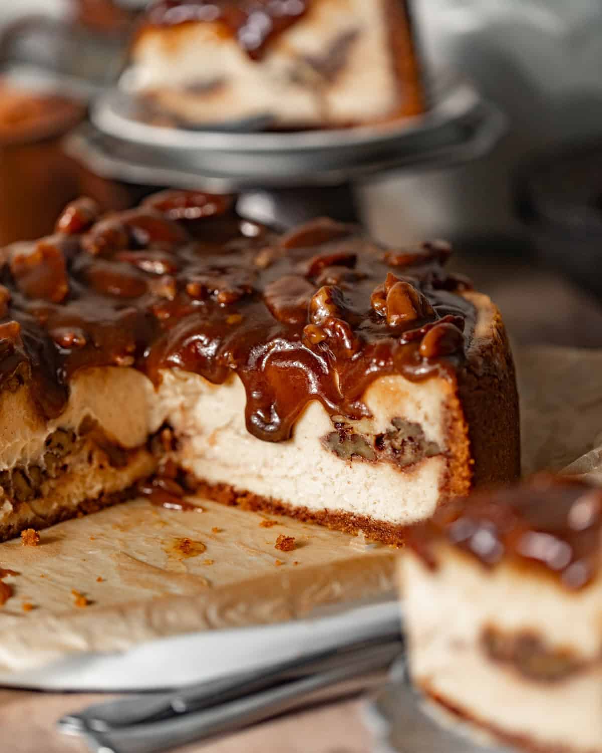 pecan pie cheesecake sliced on a serving dish with a spoon.