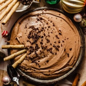 hot cocoa dip in a serving bowl with chocolate shavings on top surrounded by christmas ornaments.