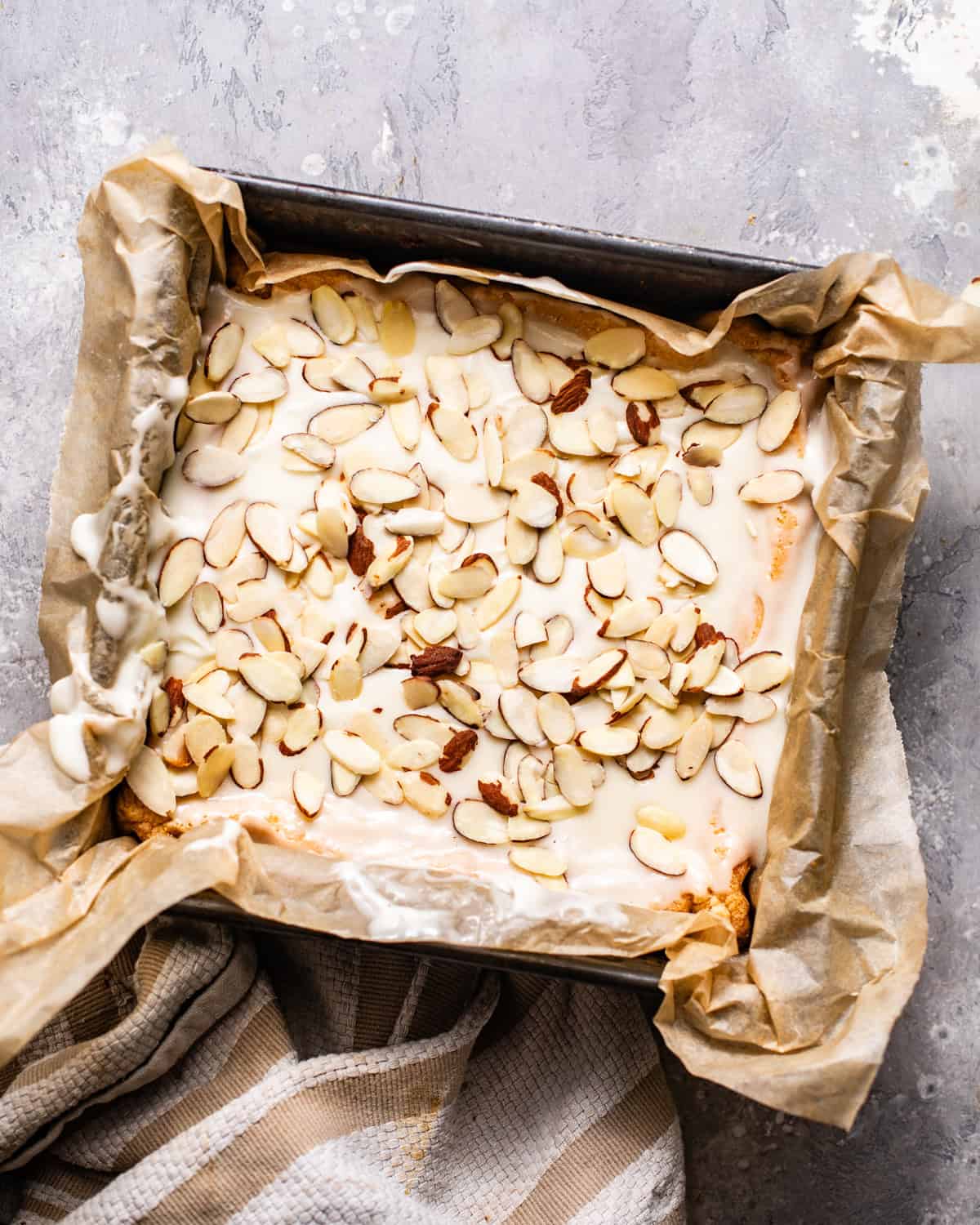 almond shortbread cookie bars in a square baking pan topped with almond glaze and sliced almonds.