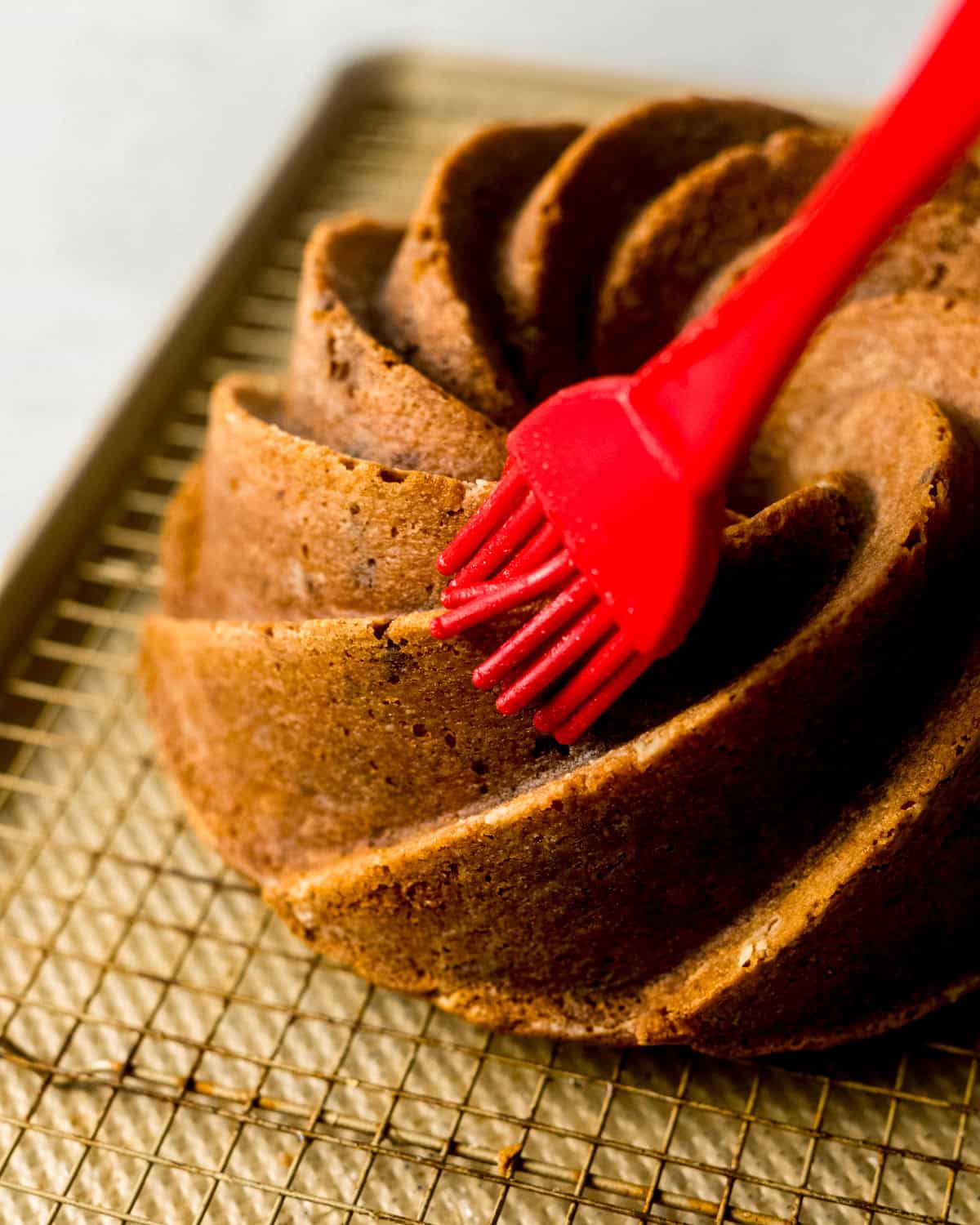 a pastry brush brushing vanilla bean simple syrup onto the biscoff cake.