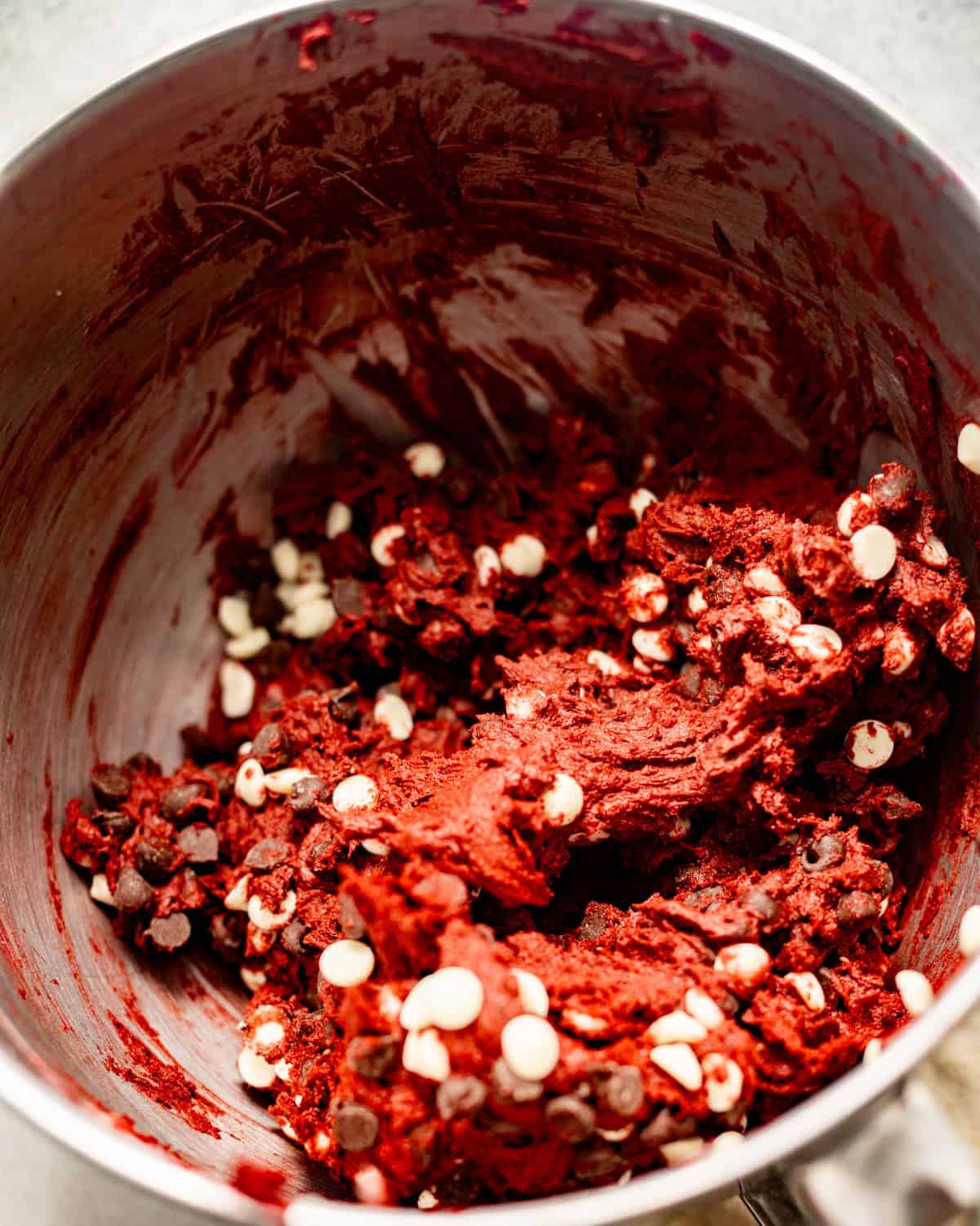red velvet cookies dough in the bowl of a stand mixer with white chocolate and semi sweet chocolate chips folded into the dough. 