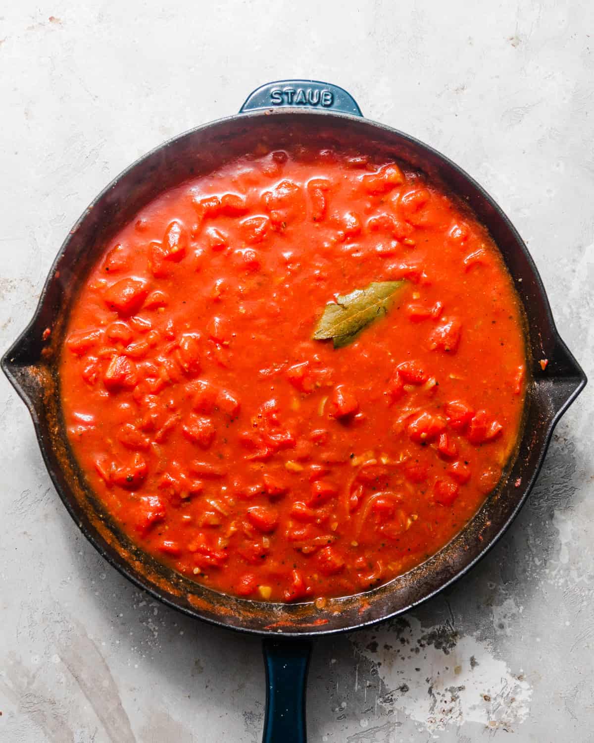 tomato and white wine sauce in a skillet with a bay leaf. 