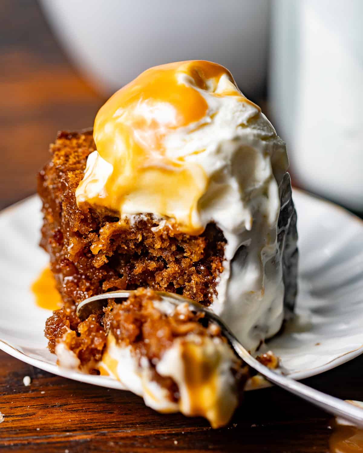a spoon scooping sticky toffee pudding cake with toffee sauce and ice cream melting into the cake.