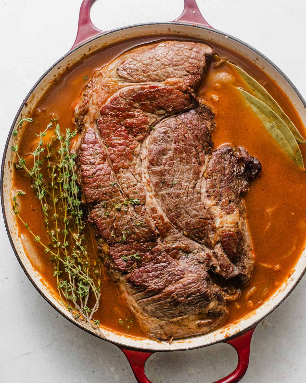 chuck roast in the pot with thyme, caramelized onions, whiskey, red wine, and bay leaves. 