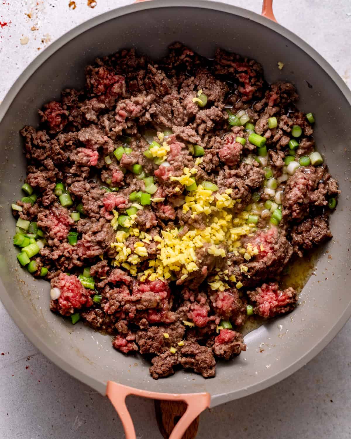 ground beef in a skillet with garlic, ginger, and scallions. 