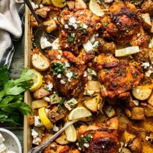 sheet pan chicken thighs and potatoes on a baking sheet with serving forks and garnished with feta and fresh parsley.