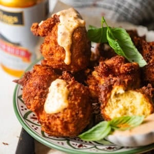 crab beignets on a plate with remoulade sauce drizzled on top.