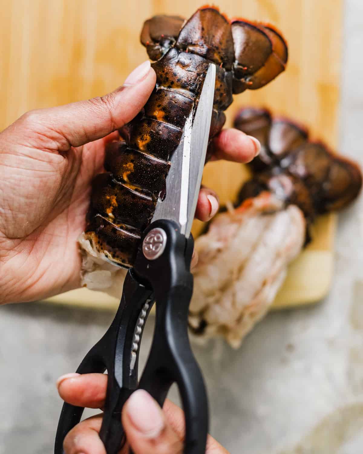 kitchen shears cutting down the top of a lobster tail to remove the meat.