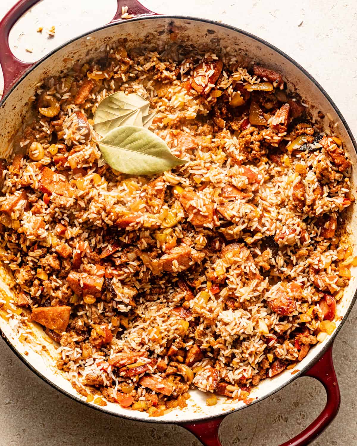 dirty rice in a pot with bay leaves, simmering in chicken broth.