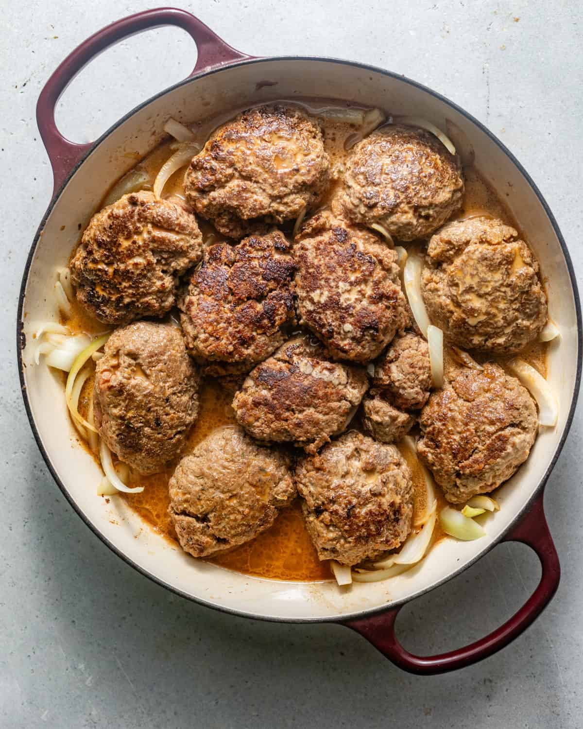 hamburger steaks in a pan with onions and gravy. 