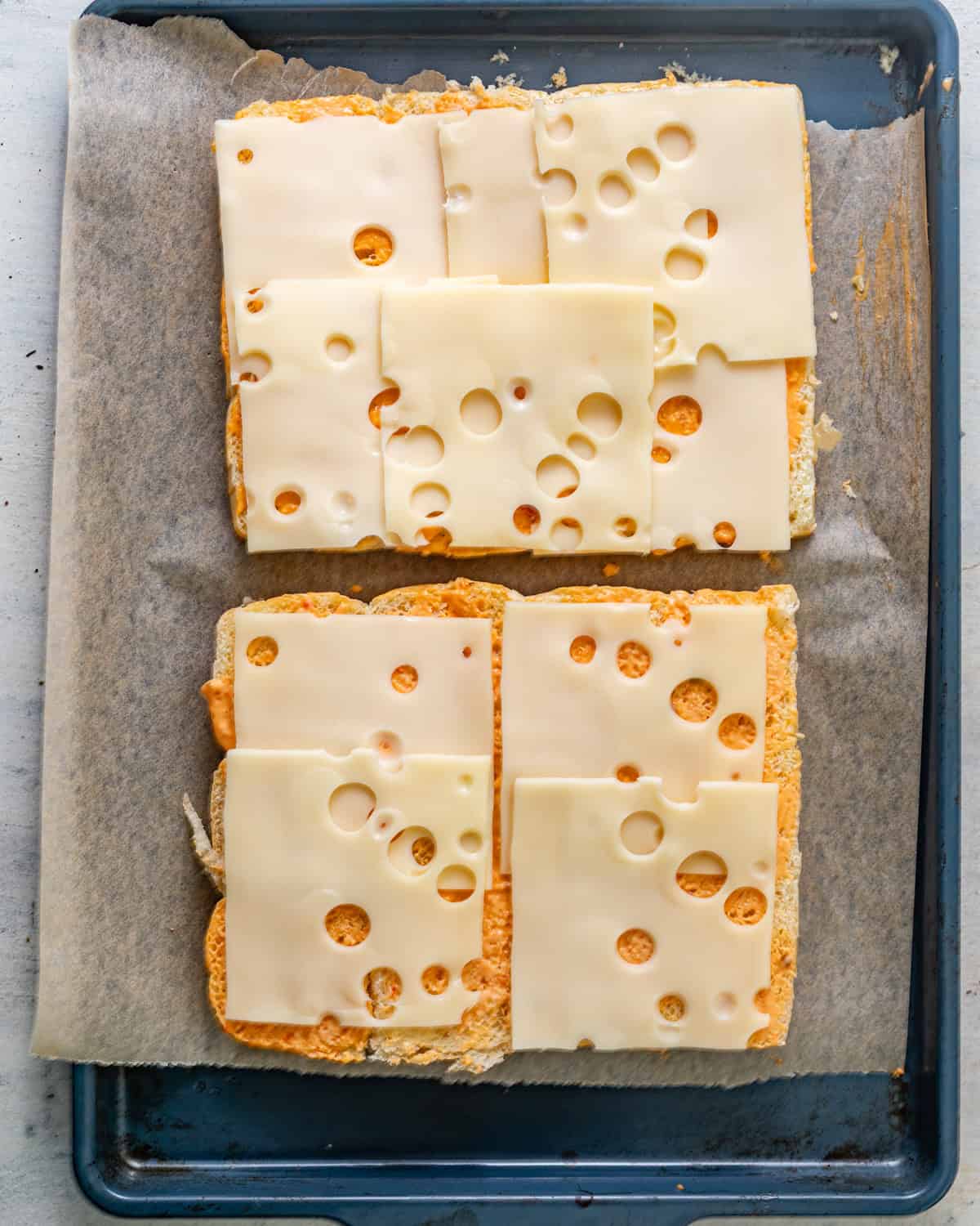 hawaiian rolls cut in half with thousand island and swiss cheese slices on top. 
