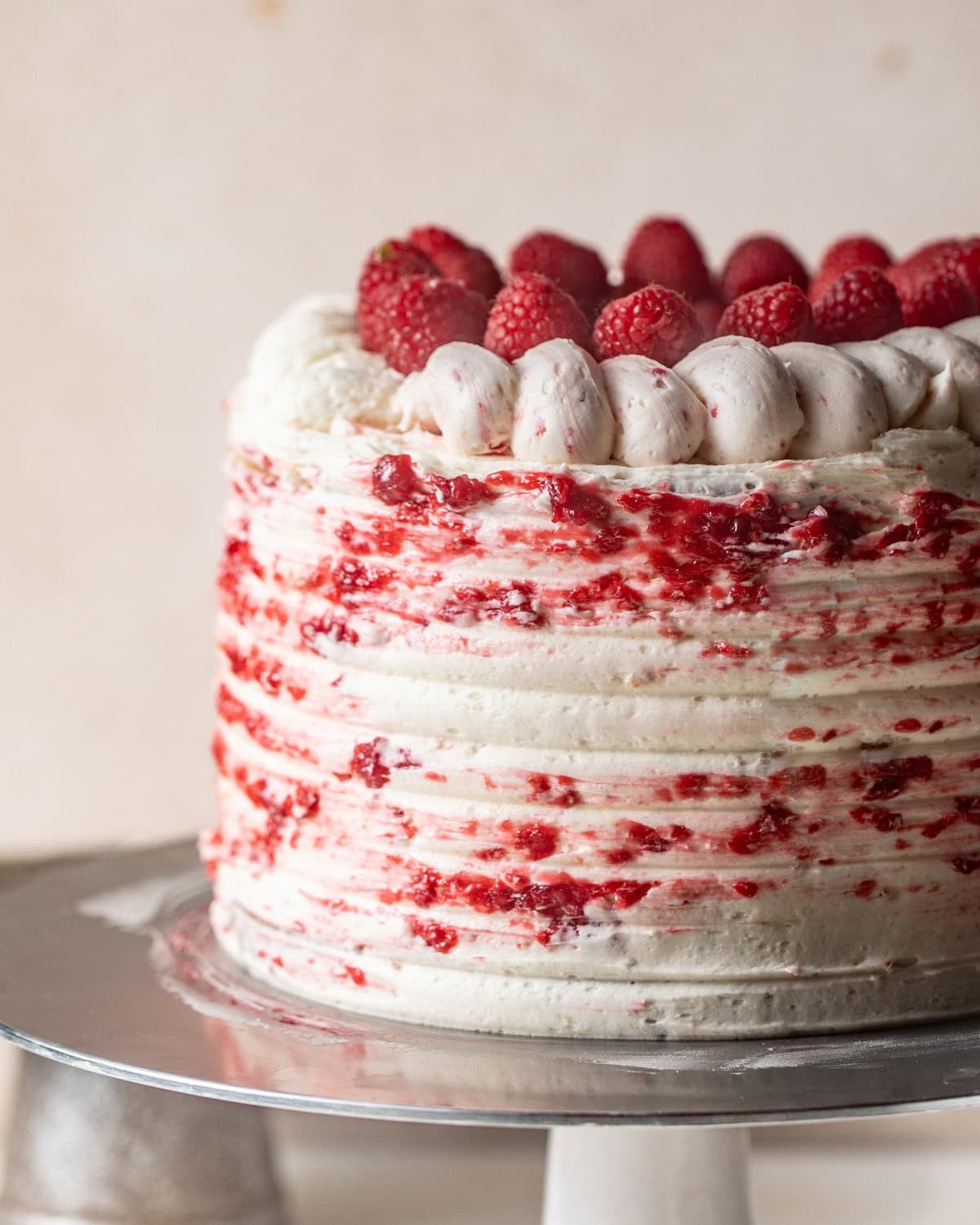 white chocolate raspberry cake on a cake stand topped with fresh raspberries and a raspberry swirl.