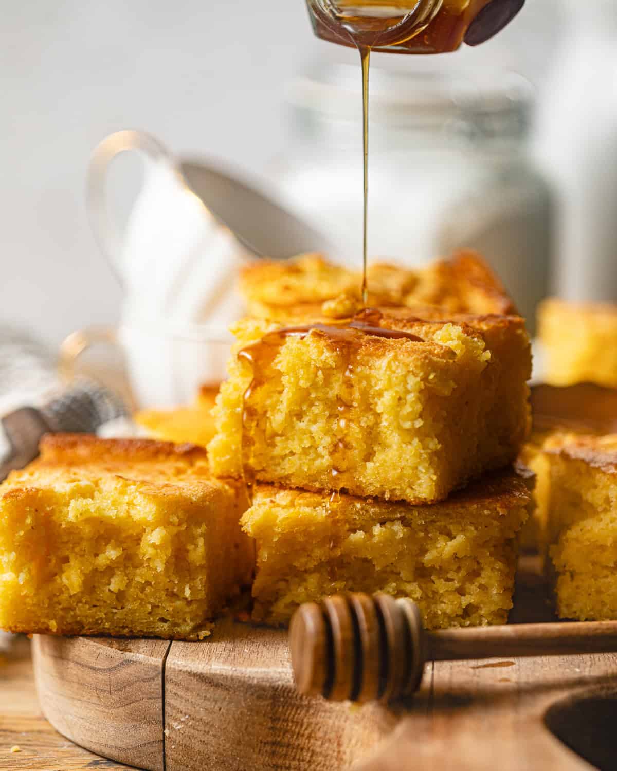 sliced jiffy cornbread stacked on top of each other with honey being poured on top. 