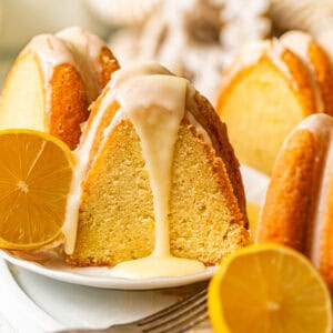 a slice of lemon ricotta pound cake on a plate with sliced lemons and lemon glaze being poured on top.
