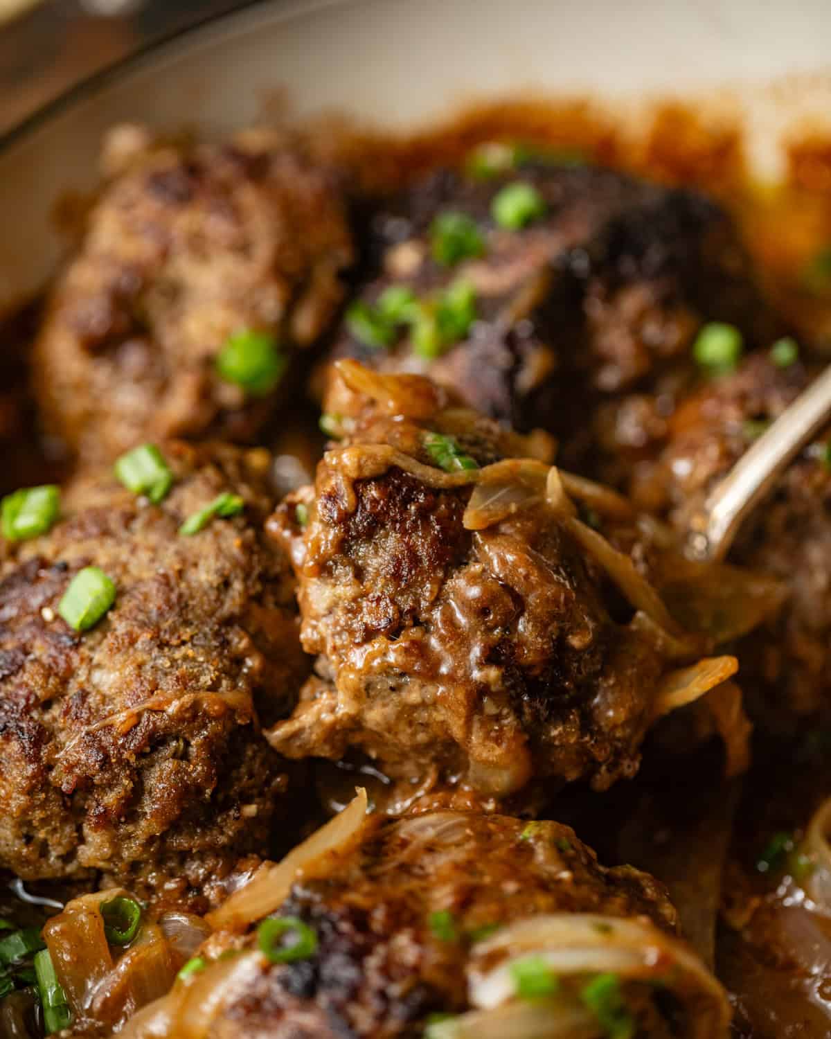 up close photo of hamburger steaks in a pan with a serving spoon. 
