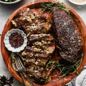 steak au poivre on a cutting board with peppercorns in a bowl and salad in a separate bowl.