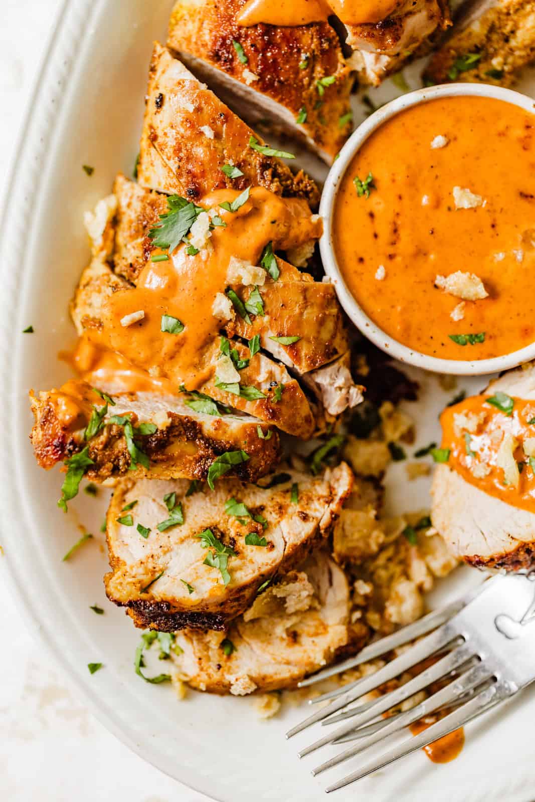 sliced pork tenderloin on a plate with cajun sauce in a small bowl. 