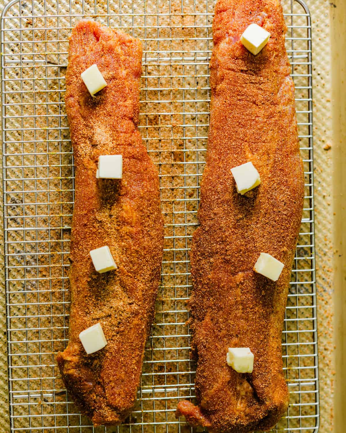 seasoned pork tenderloin on a wire rack with a few pats of butter on top. 