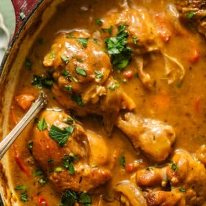 smothered chicken in a pot with a serving spoon with fresh parsley garnish on top.