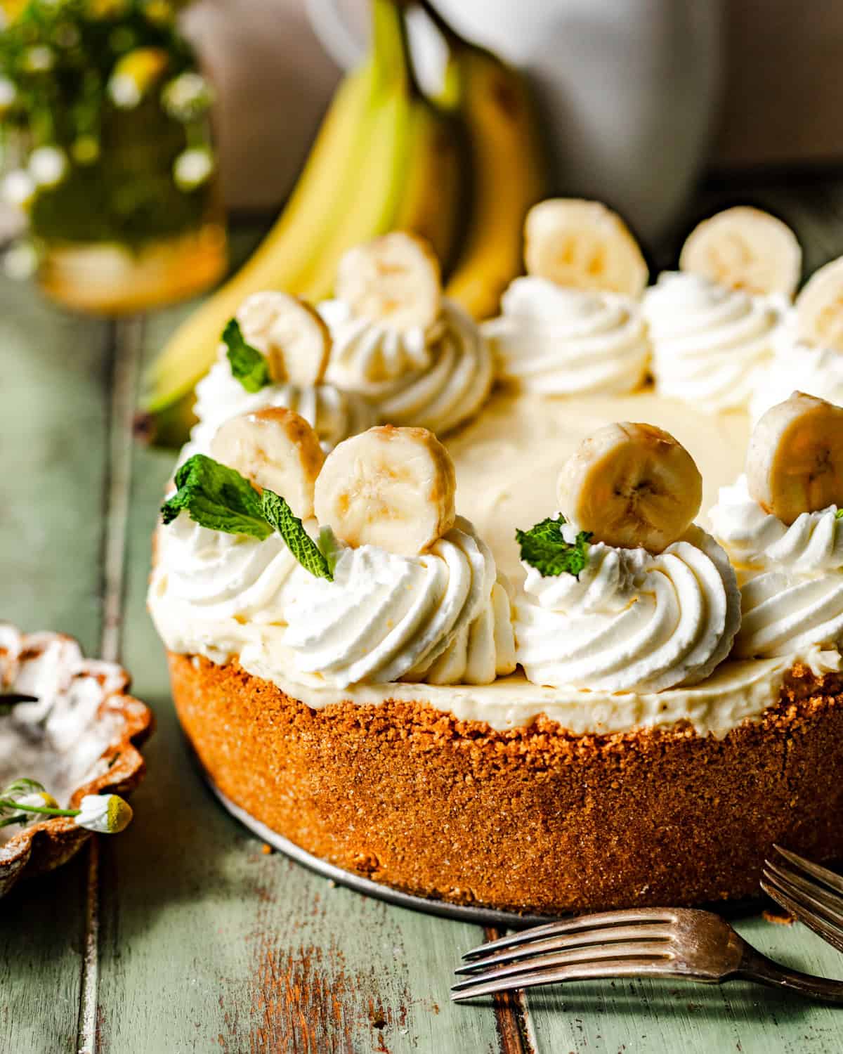 banana cream pie on a green surface with a fork and a bunch of bananas in the background.